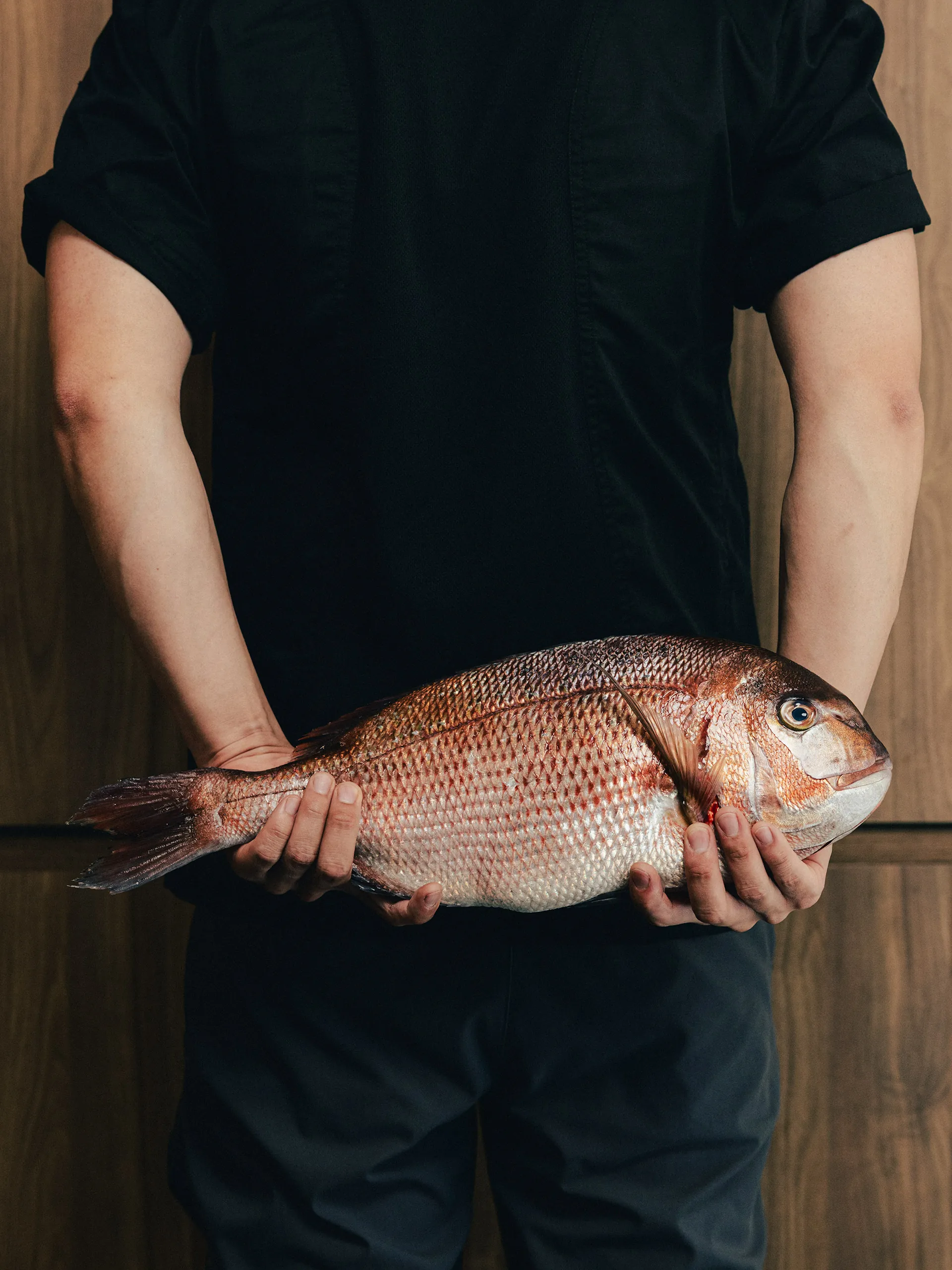 A Zumi chef holding a whole sea bream